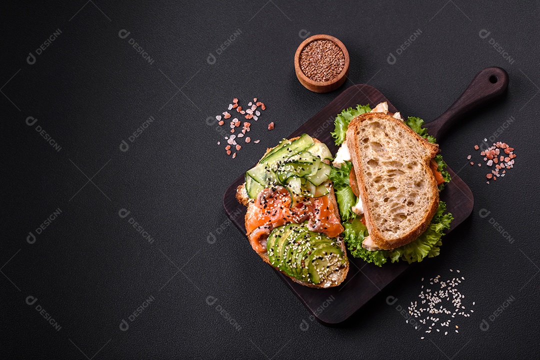 Sanduíche fresco e saboroso com salmão, abacate e sementes de gergelim e linho sobre um fundo escuro de concreto