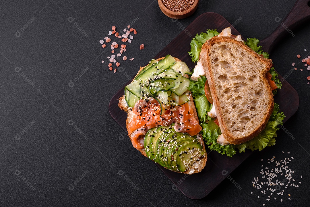 Sanduíche fresco e saboroso com salmão, abacate e sementes de gergelim e linho sobre um fundo escuro de concreto