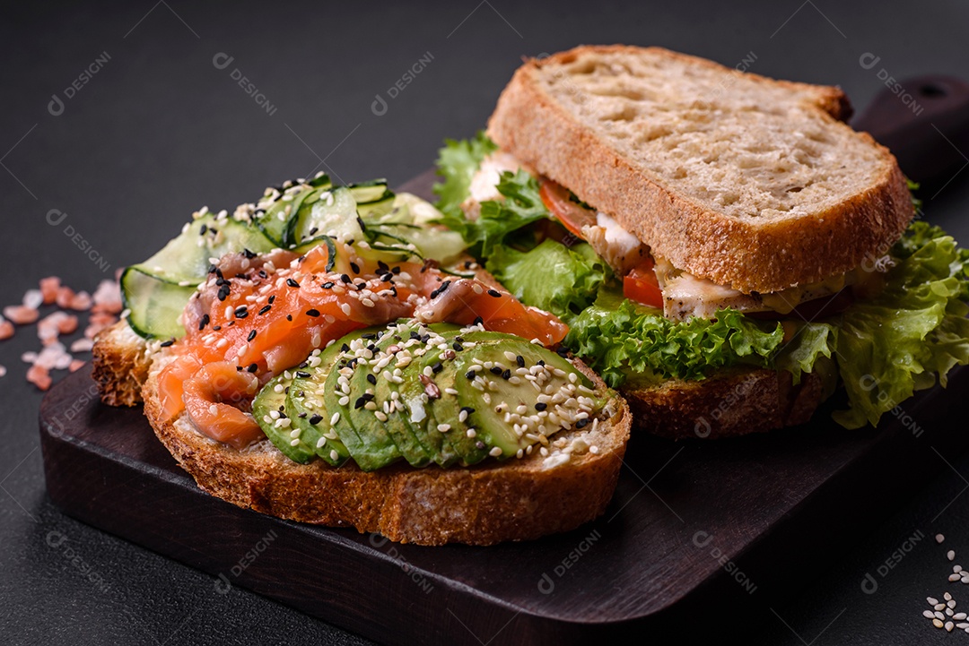 Sanduíche fresco e saboroso com salmão, abacate e sementes de gergelim e linho sobre um fundo escuro de concreto