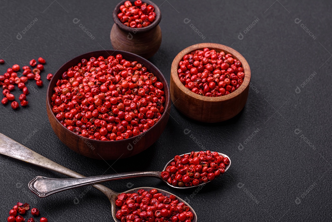 Especiarias, ervilhas de pimenta da Jamaica na cor vermelha ou rosa em uma tigela de madeira sobre um fundo preto de concreto. Cozinha asiática