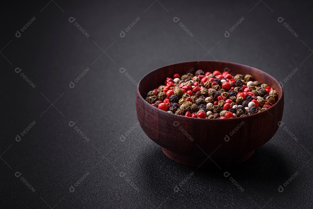 Pimenta da Jamaica de cores diferentes, rosa, branco, verde, não moída em um pires de madeira sobre um fundo escuro de concreto