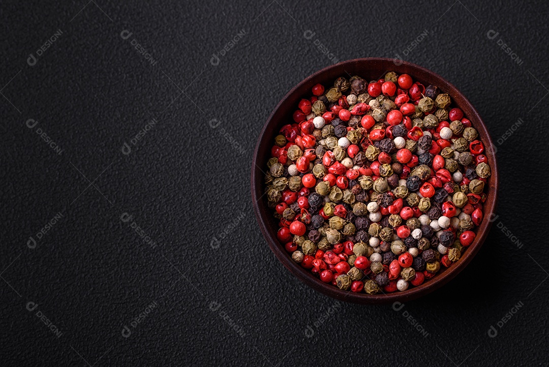 Pimenta da Jamaica de cores diferentes, rosa, branco, verde, não moída em um pires de madeira sobre um fundo escuro de concreto