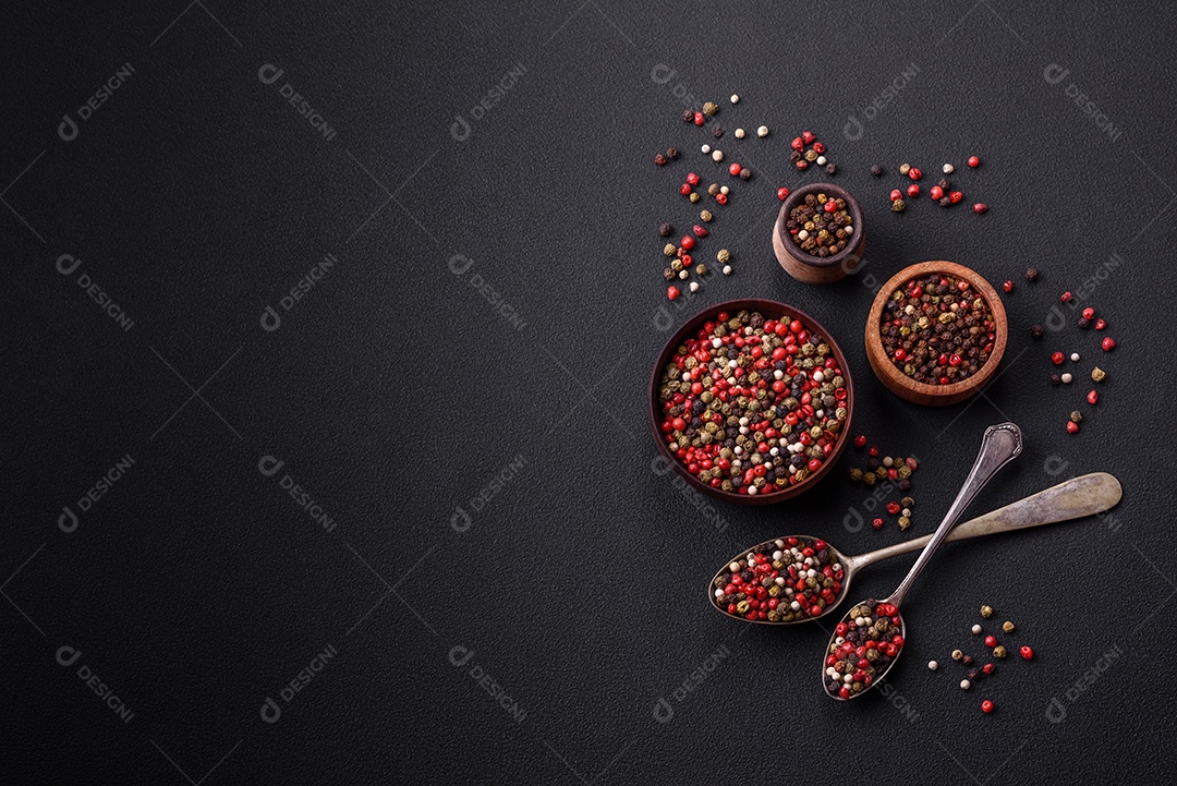 Pimenta da Jamaica de cores diferentes, rosa, branco, verde, não moída em um pires de madeira sobre um fundo escuro de concreto