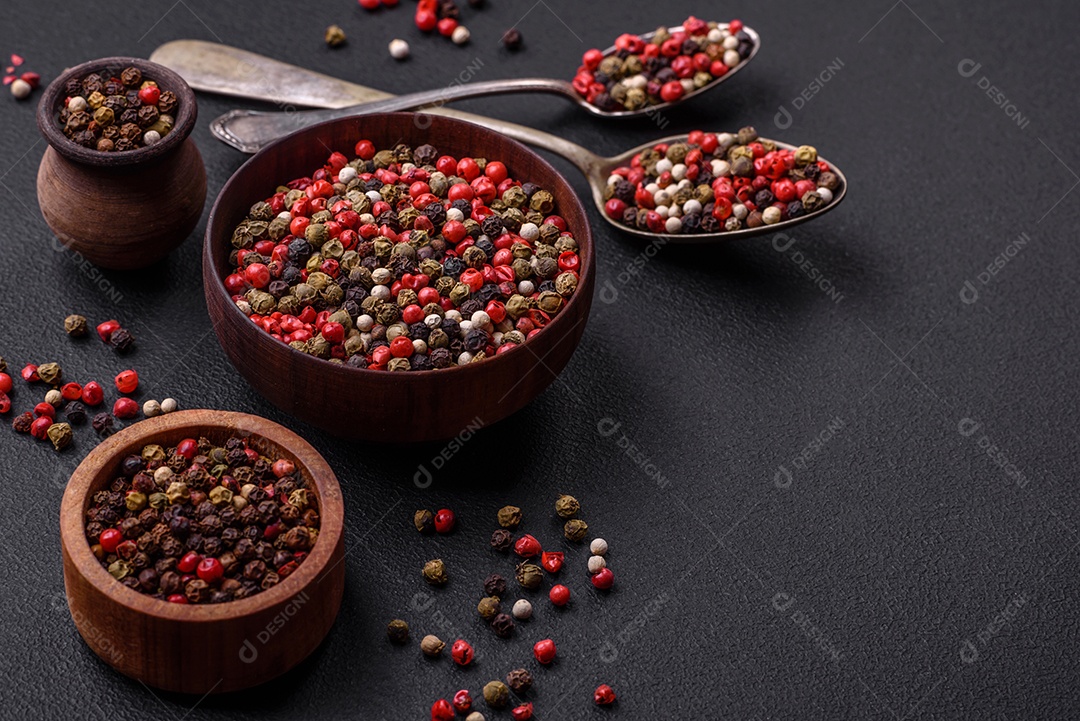 Pimenta da Jamaica de cores diferentes, rosa, branco, verde, não moída em um pires de madeira sobre um fundo escuro de concreto