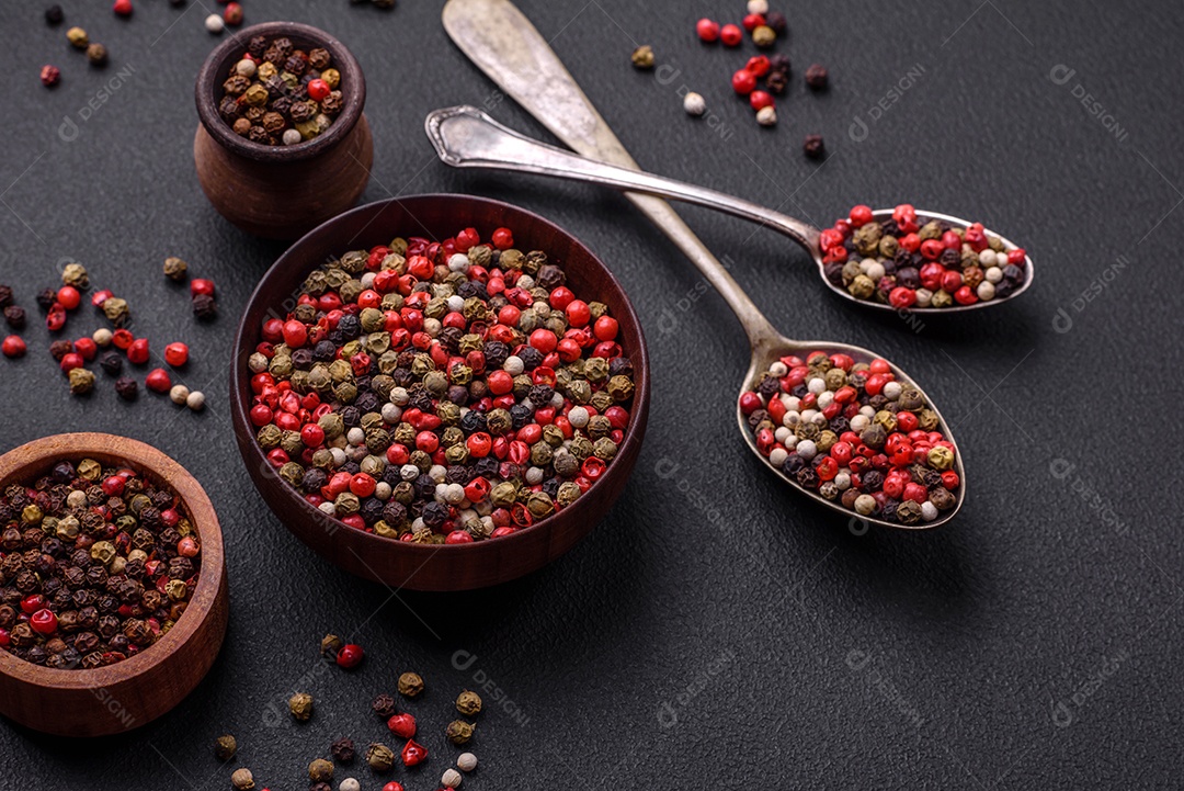 Pimenta da Jamaica de cores diferentes, rosa, branco, verde, não moída em um pires de madeira sobre um fundo escuro de concreto