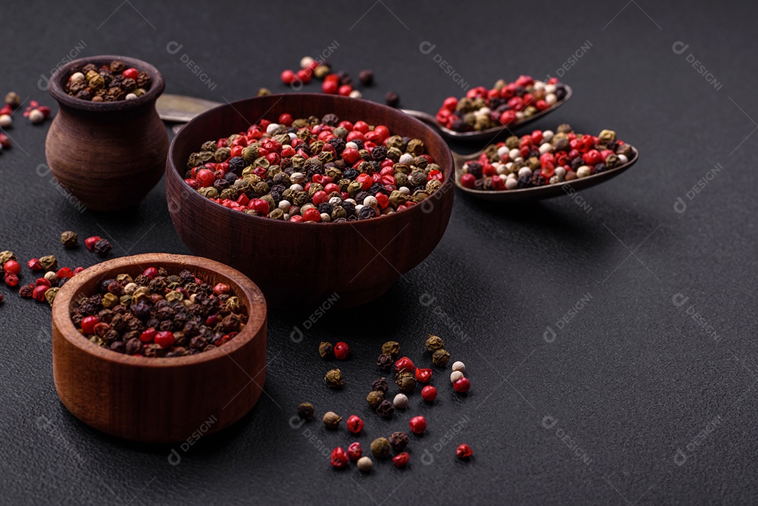Pimenta da Jamaica de cores diferentes, rosa, branco, verde, não moída em um pires de madeira sobre um fundo escuro de concreto