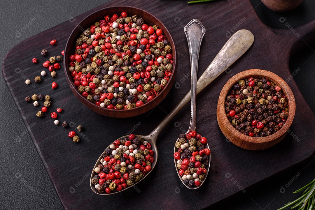 Pimenta da Jamaica de cores diferentes, rosa, branco, verde, não moída em um pires de madeira sobre um fundo escuro de concreto