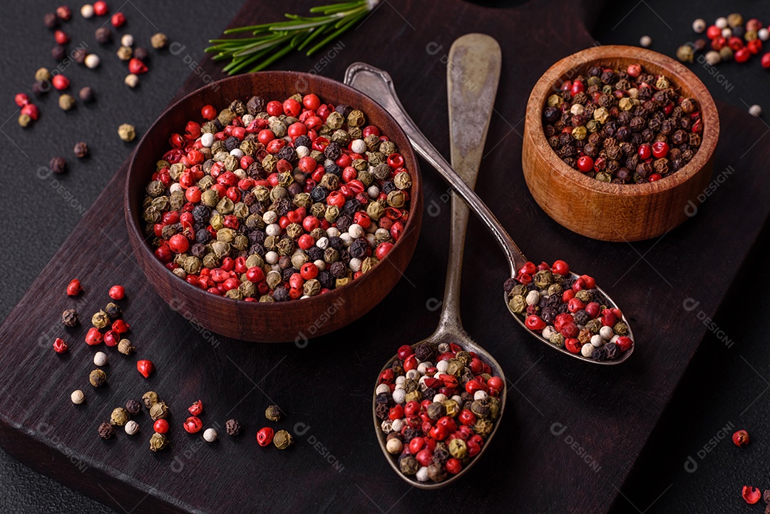 Pimenta da Jamaica de cores diferentes, rosa, branco, verde, não moída em um pires de madeira sobre um fundo escuro de concreto