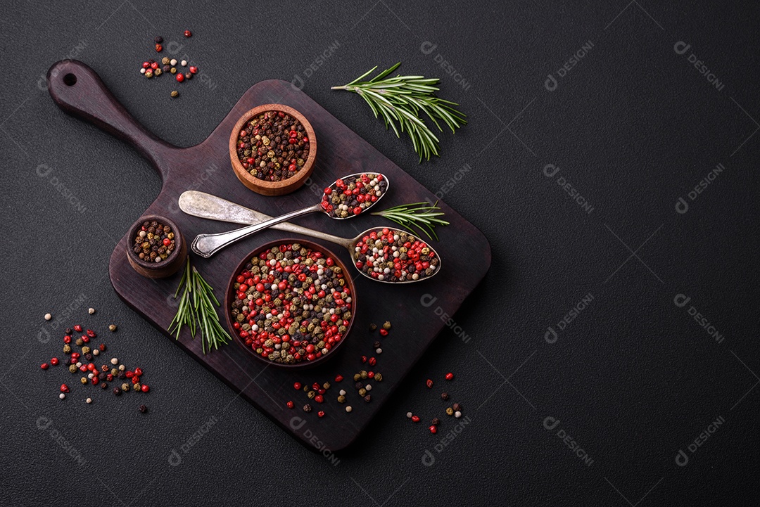 Pimenta da Jamaica de cores diferentes, rosa, branco, verde, não moída em um pires de madeira sobre um fundo escuro de concreto