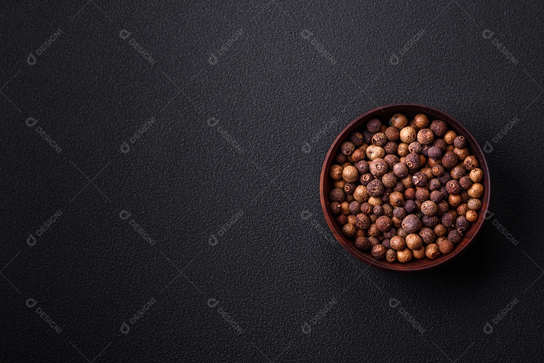 Especiaria de cor marrom pimenta da Jamaica não moída em um pires de madeira sobre um fundo escuro de concreto