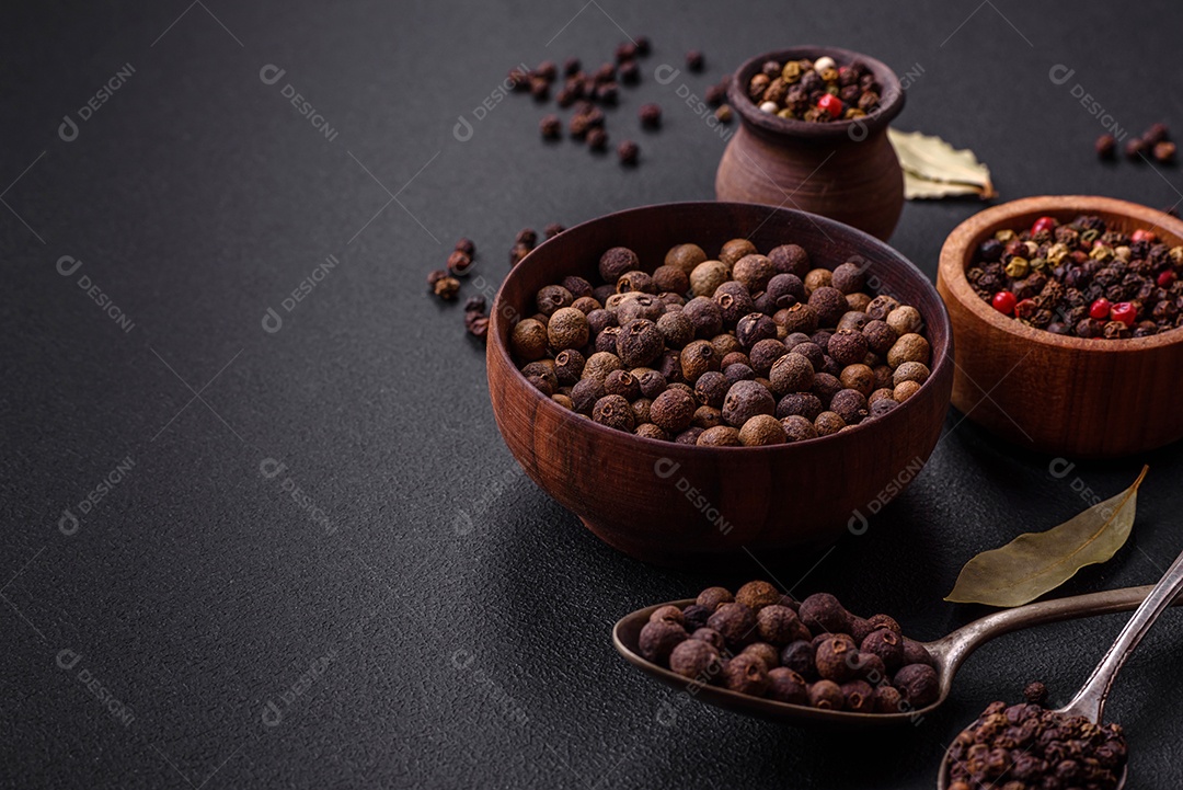 Especiaria de cor marrom pimenta da Jamaica não moída em um pires de madeira sobre um fundo escuro de concreto