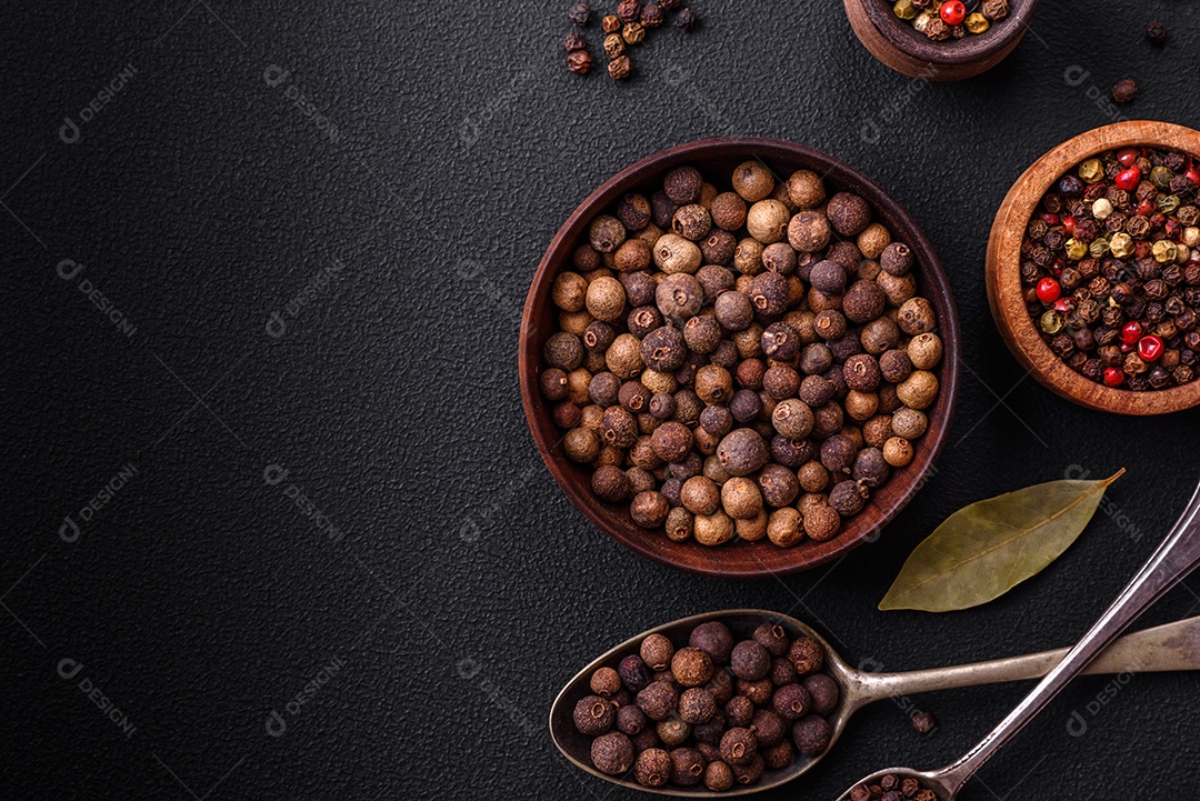 Especiaria de cor marrom pimenta da Jamaica não moída em um pires de madeira sobre um fundo escuro de concreto