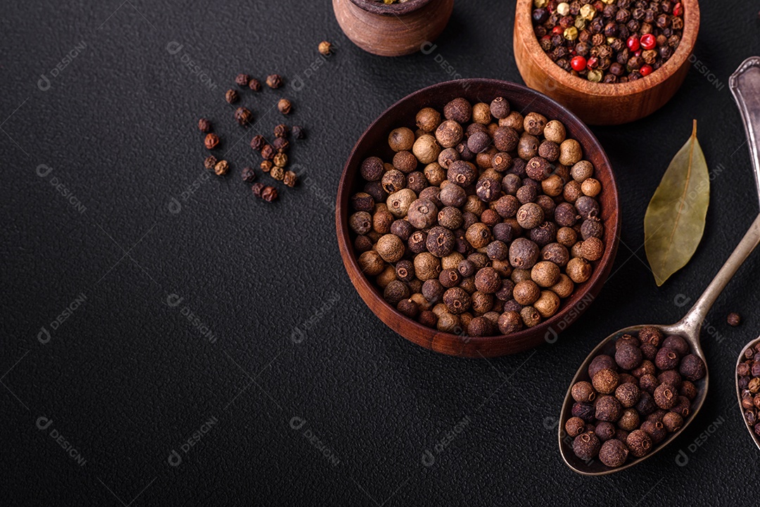 Especiaria de cor marrom pimenta da Jamaica não moída em um pires de madeira sobre um fundo escuro de concreto
