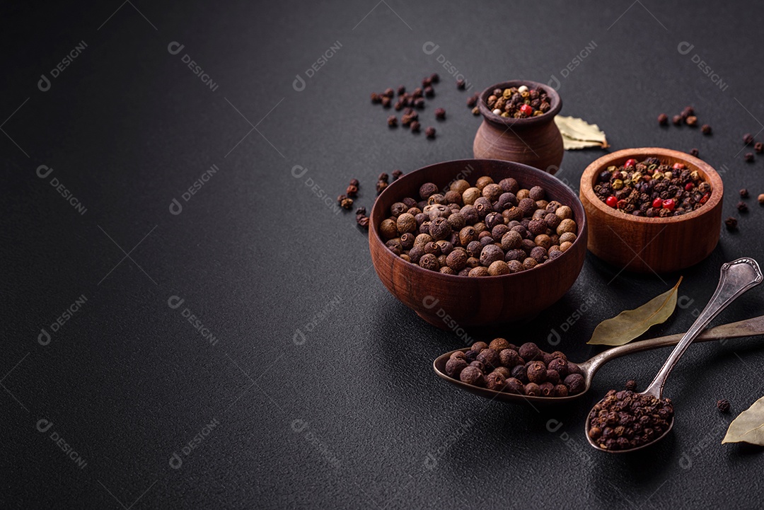 Especiaria de cor marrom pimenta da Jamaica não moída em um pires de madeira sobre um fundo escuro de concreto