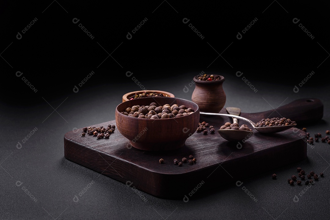 Especiaria de cor marrom pimenta da Jamaica não moída em um pires de madeira sobre um fundo escuro de concreto