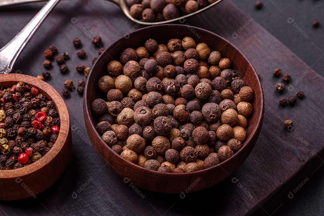 Especiaria de cor marrom pimenta da Jamaica não moída em um pires de madeira sobre um fundo escuro de concreto