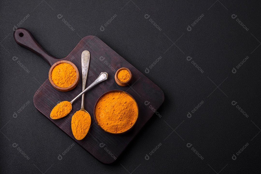 Cúrcuma amarela brilhante ou tempero de curry para preparação de alimentos asiáticos em fundo escuro de concreto