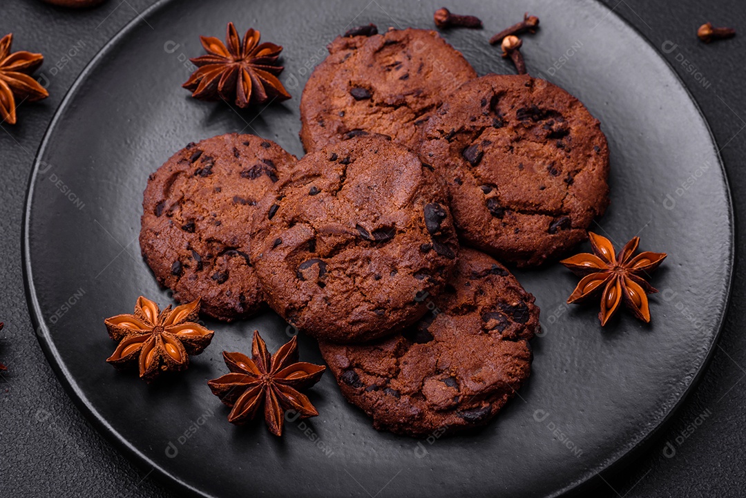 Deliciosos biscoitos de chocolate com nozes em uma placa de cerâmica preta sobre um fundo escuro de concreto