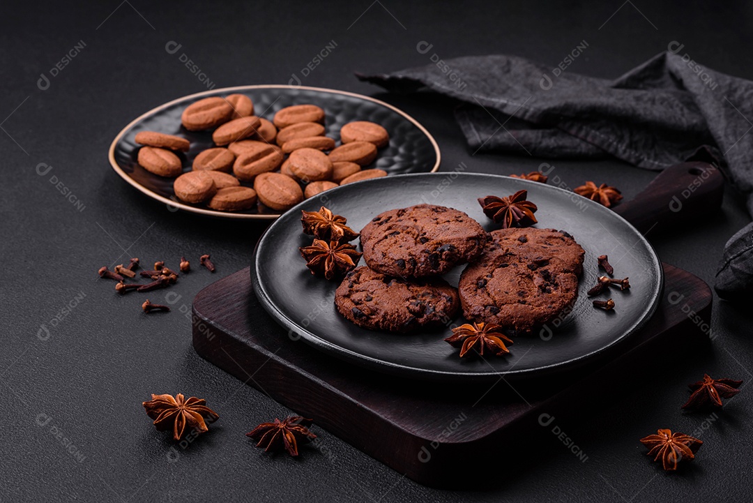 Deliciosos biscoitos de chocolate com anis e grãos de café em uma placa de cerâmica preta sobre um fundo escuro de concreto