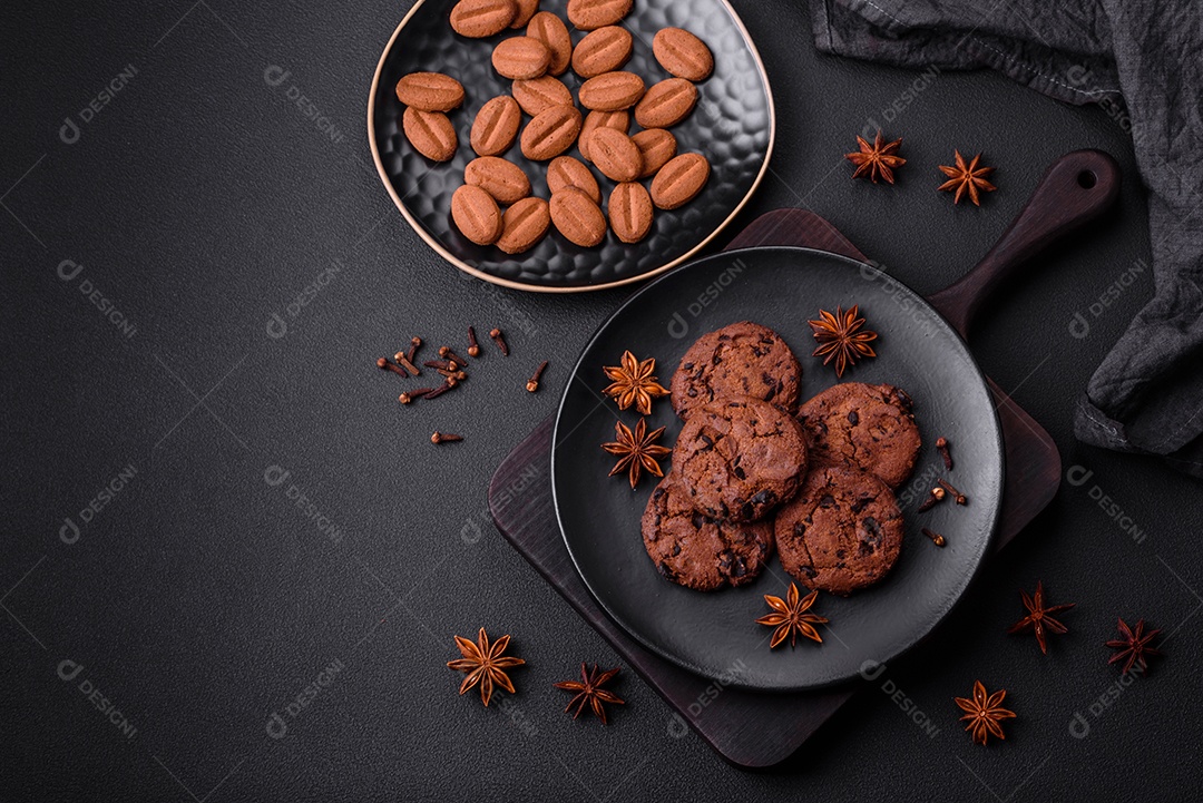 Deliciosos biscoitos de chocolate com anis e grãos de café em uma placa de cerâmica preta sobre um fundo escuro de concreto