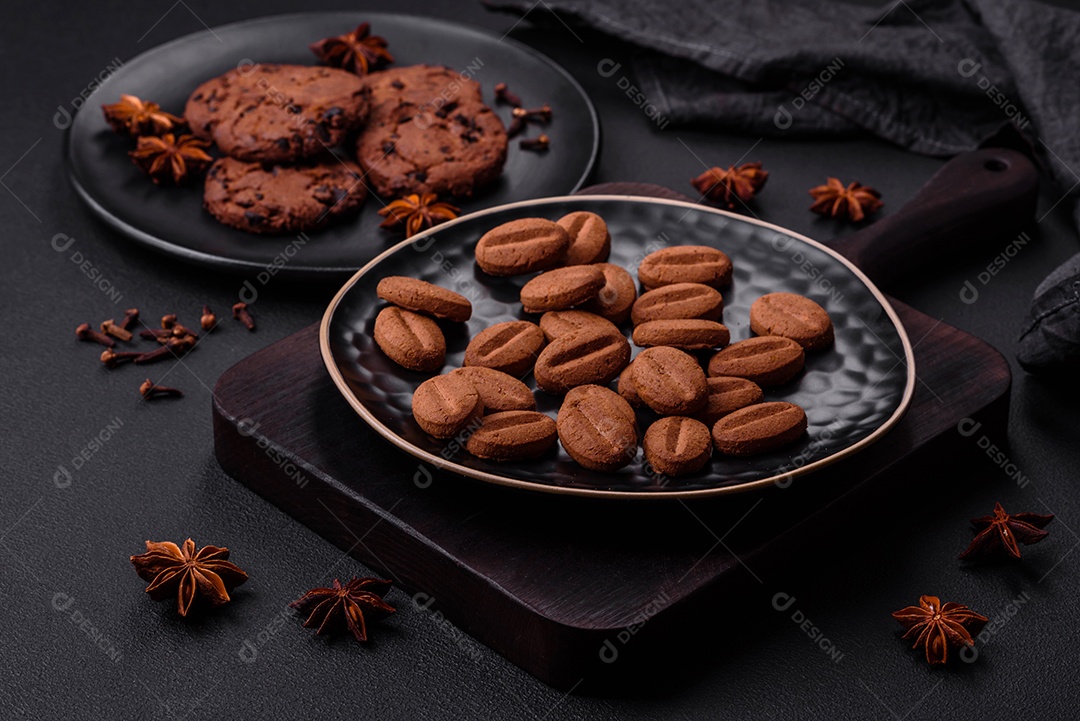 Deliciosos biscoitos de chocolate com anis e grãos de café em uma placa de cerâmica preta sobre um fundo escuro de concreto
