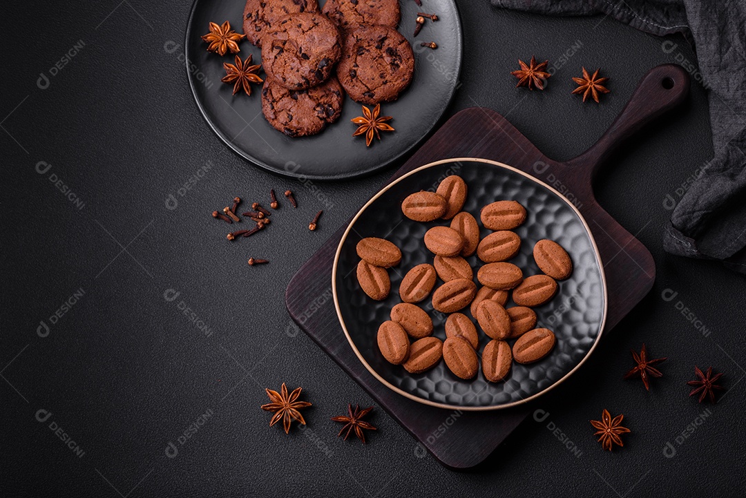 Deliciosos biscoitos de chocolate com anis e grãos de café em uma placa de cerâmica preta sobre um fundo escuro de concreto