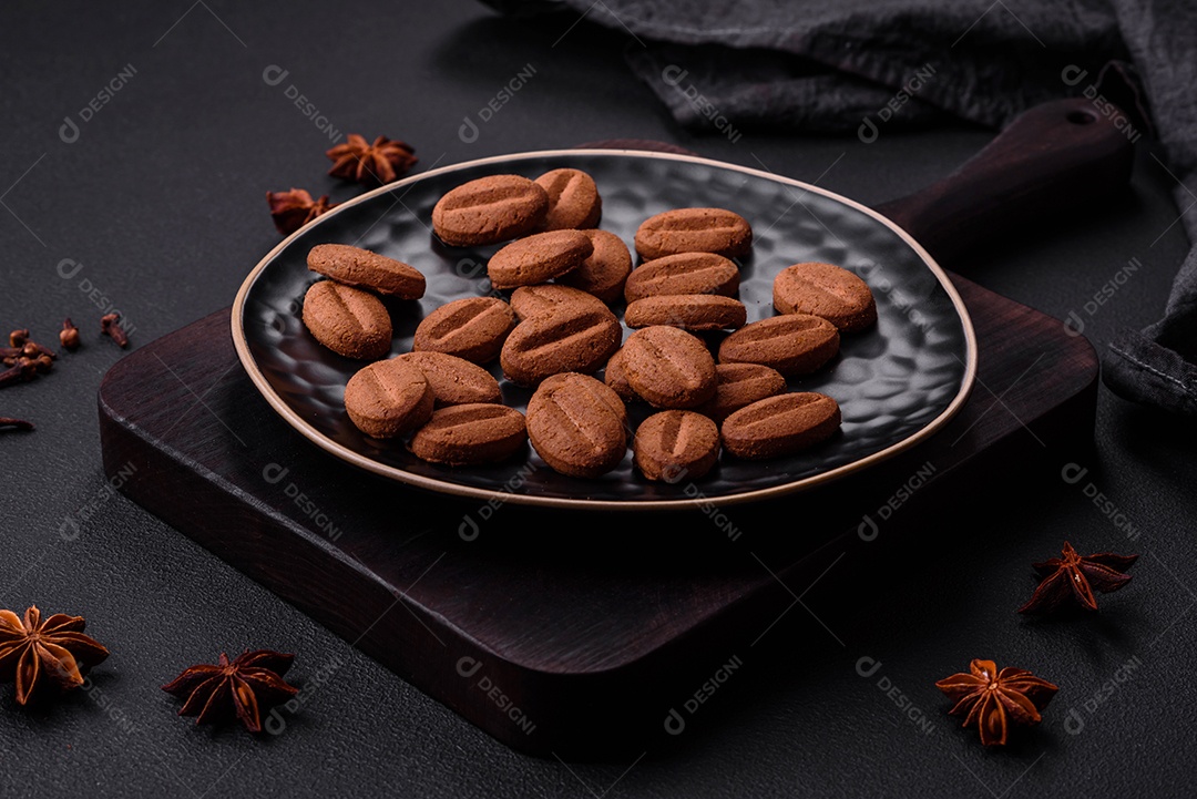 Grãos de café e anis estrelado em uma placa de cerâmica preta sobre um fundo escuro.