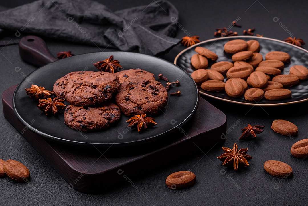 Grãos de café e anis estrelado em uma placa de cerâmica preta sobre um fundo escuro.