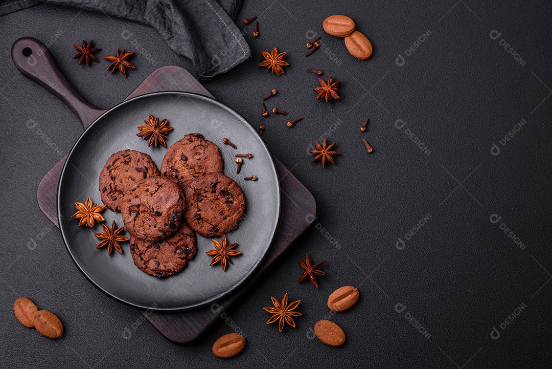 Deliciosos biscoitos de chocolate com anis e grãos de café em uma placa de cerâmica preta sobre um fundo escuro de concreto