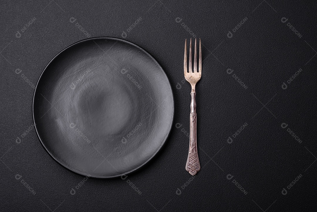 Placa redonda de cerâmica vazia em fundo de concreto texturizado escuro. Talheres, preparação para o jantar