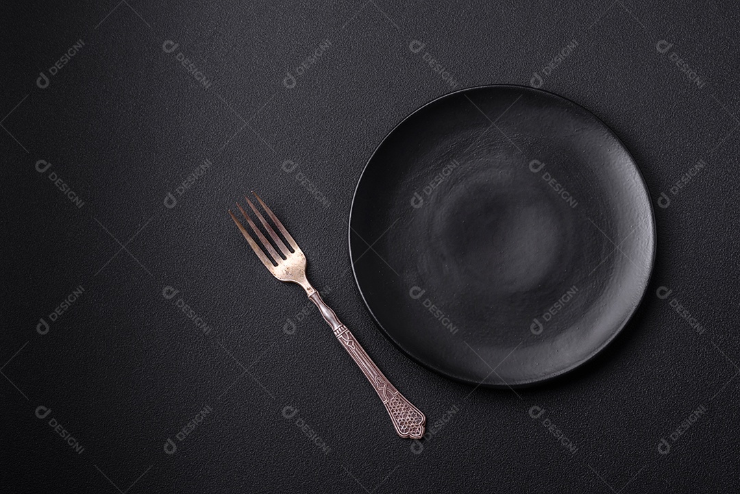 Placa redonda de cerâmica vazia em fundo de concreto texturizado escuro. Talheres, preparação para o jantar