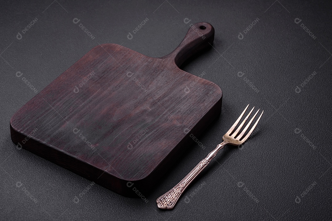 Tábua de corte de madeira vazia em fundo de concreto texturizado escuro. Talheres, preparação para o jantar