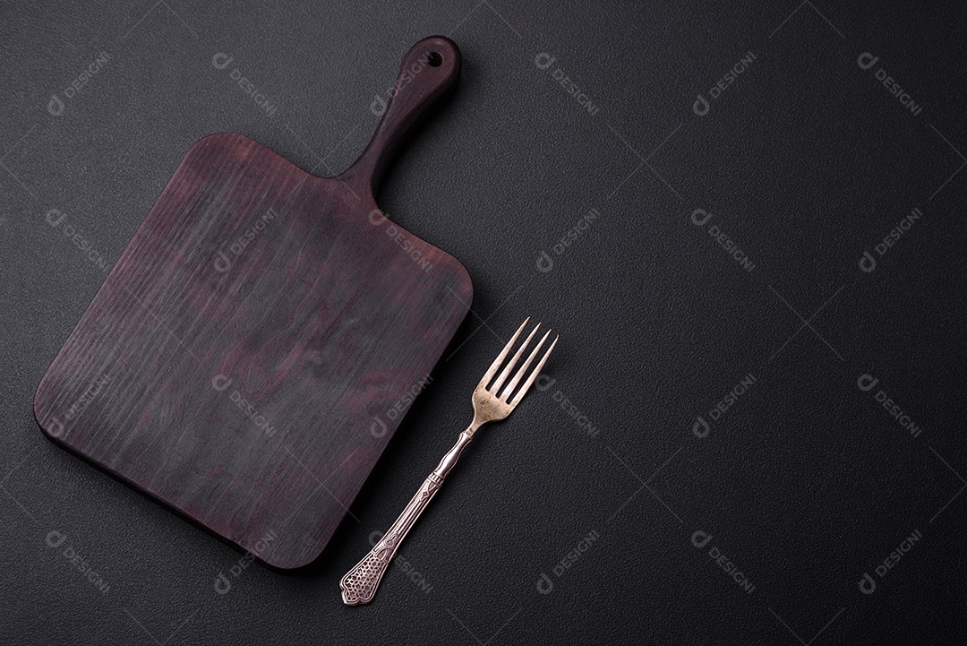 Tábua de corte de madeira vazia em fundo de concreto texturizado escuro. Talheres, preparação para o jantar