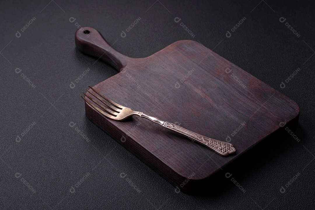 Tábua de corte de madeira vazia em fundo de concreto texturizado escuro. Talheres, preparação para o jantar