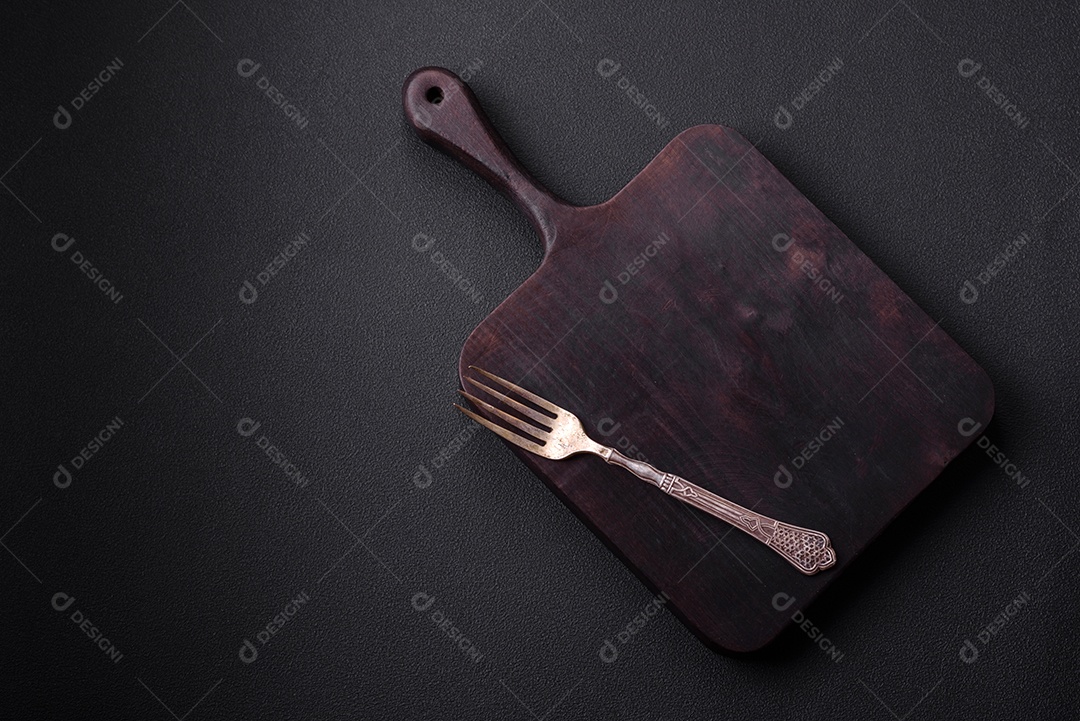 Tábua de corte de madeira vazia em fundo de concreto texturizado escuro. Talheres, preparação para o jantar