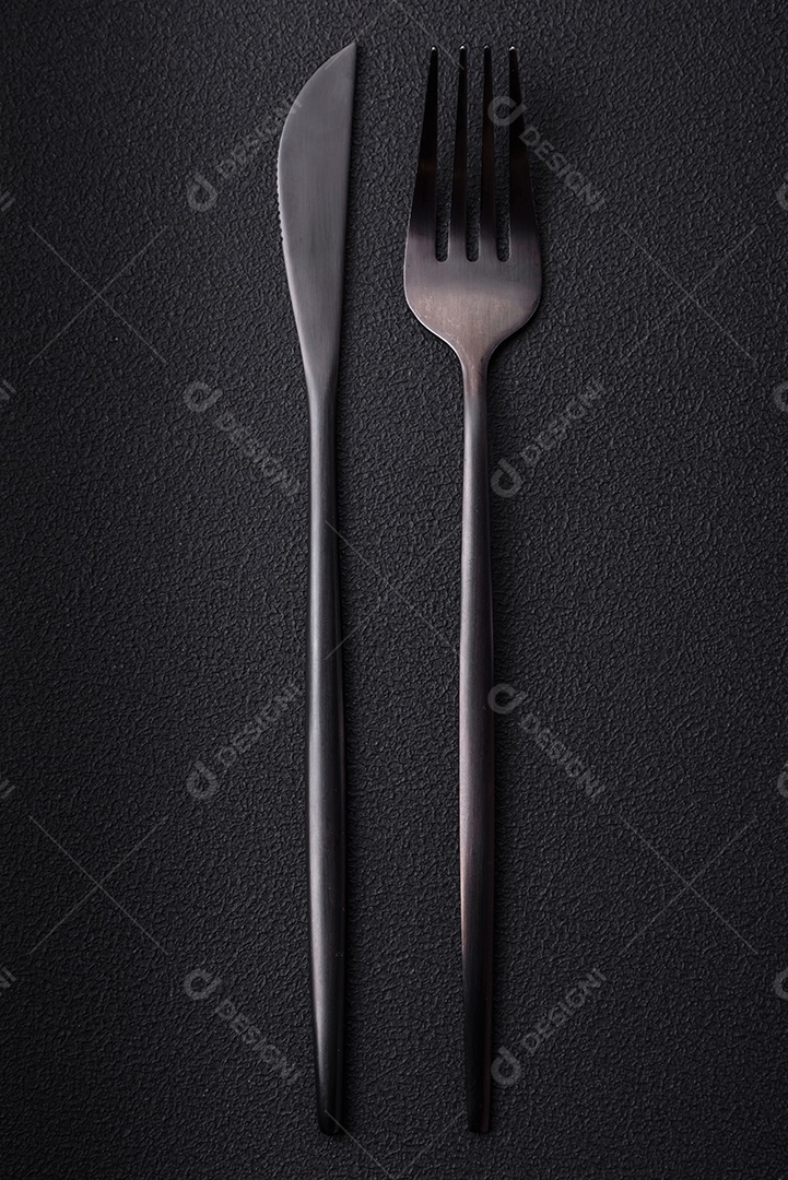 Faca e garfo de cozinha de metal em um fundo de concreto texturizado escuro. Talheres, preparação para o jantar