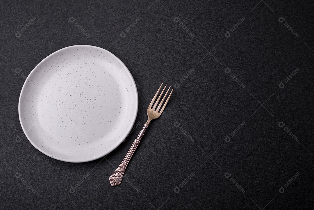 Placa redonda de cerâmica vazia em fundo de concreto texturizado escuro. Talheres, preparação para o jantar