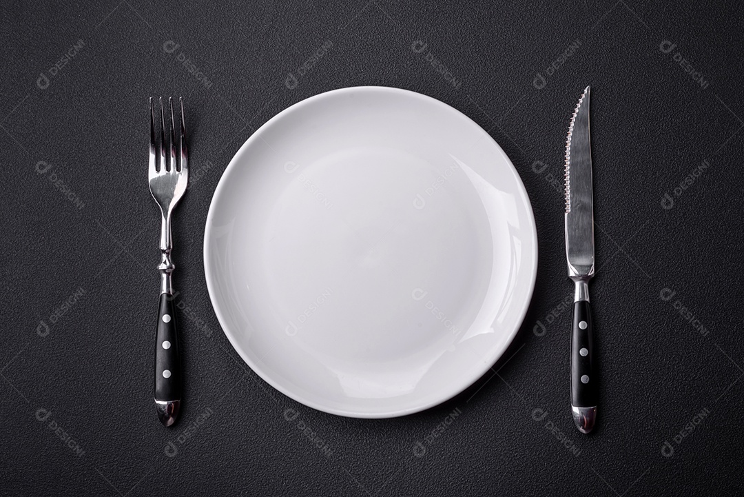 Placa redonda de cerâmica vazia em fundo de concreto texturizado escuro. Talheres, preparação para o jantar