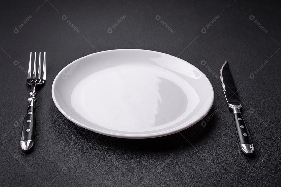 Placa redonda de cerâmica vazia em fundo de concreto texturizado escuro. Talheres, preparação para o jantar
