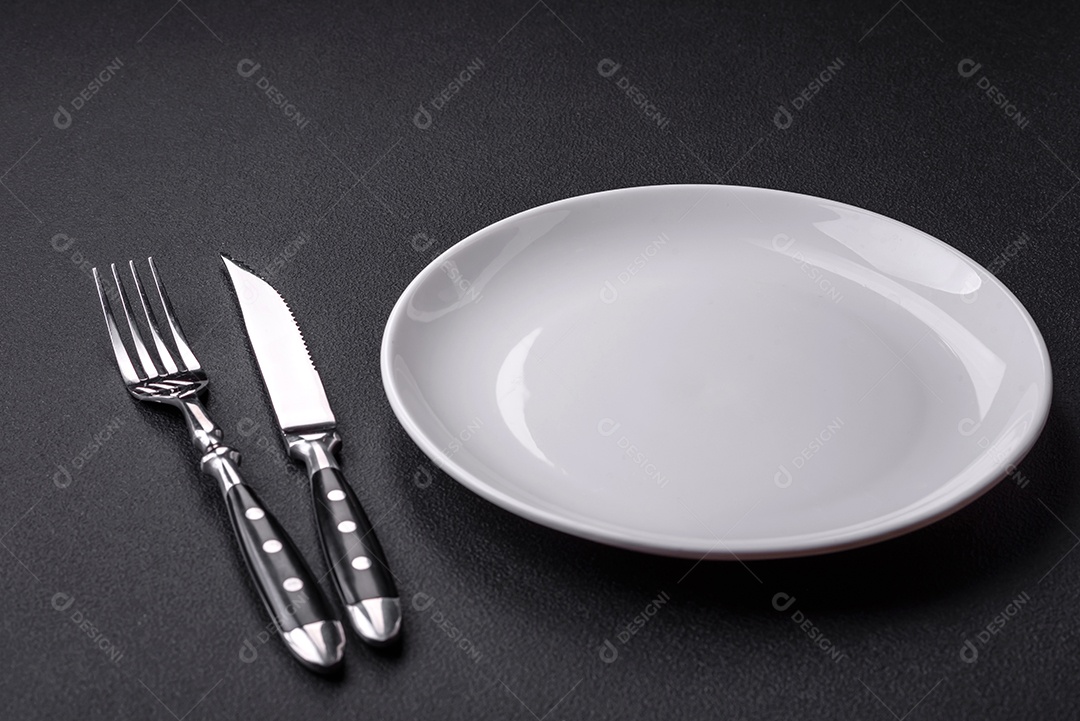 Placa redonda de cerâmica vazia em fundo de concreto texturizado escuro. Talheres, preparação para o jantar