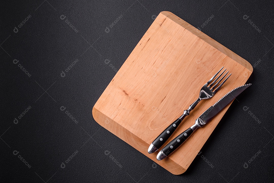 Tábua de corte de madeira vazia em fundo de concreto texturizado escuro. Talheres, preparação para o jantar