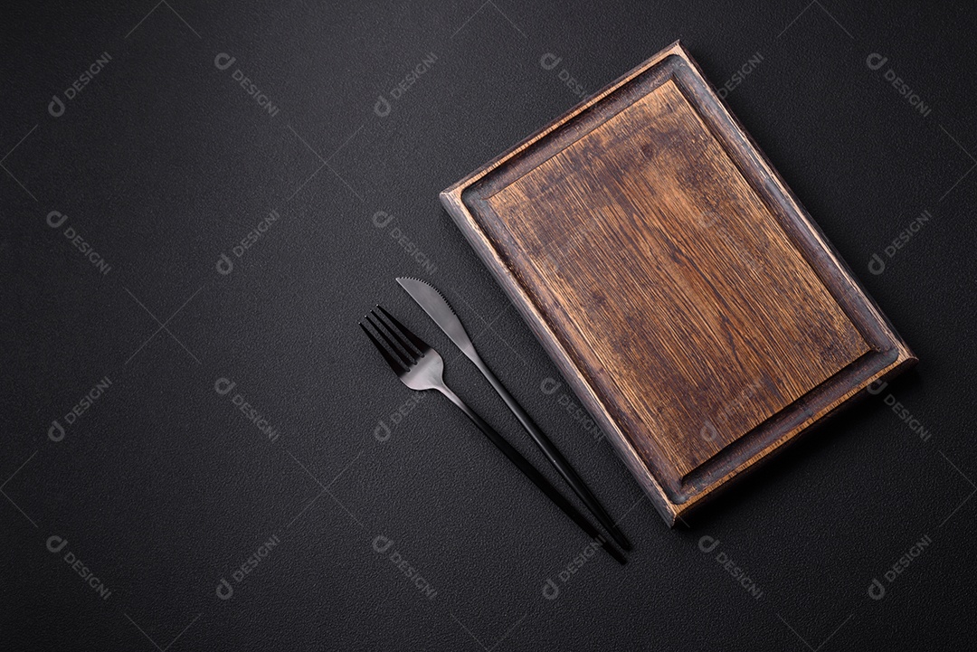 Tábua de corte de madeira vazia em fundo de concreto texturizado escuro. Talheres, preparação para o jantar