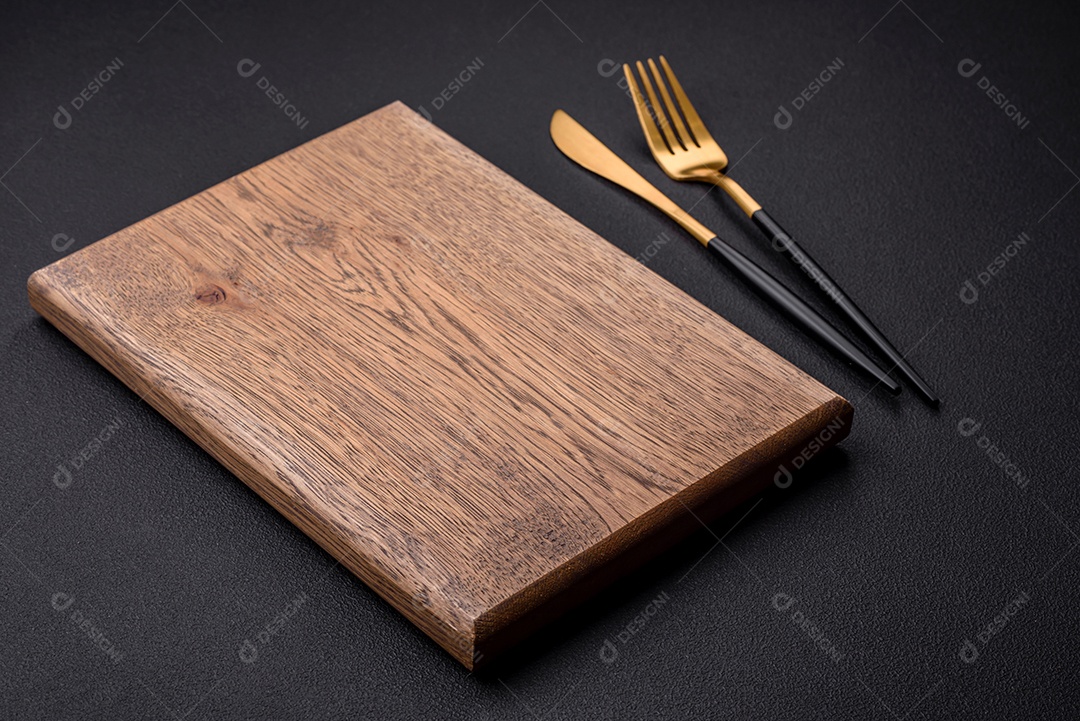 Tábua de corte de madeira vazia em fundo de concreto texturizado escuro. Talheres, preparação para o jantar