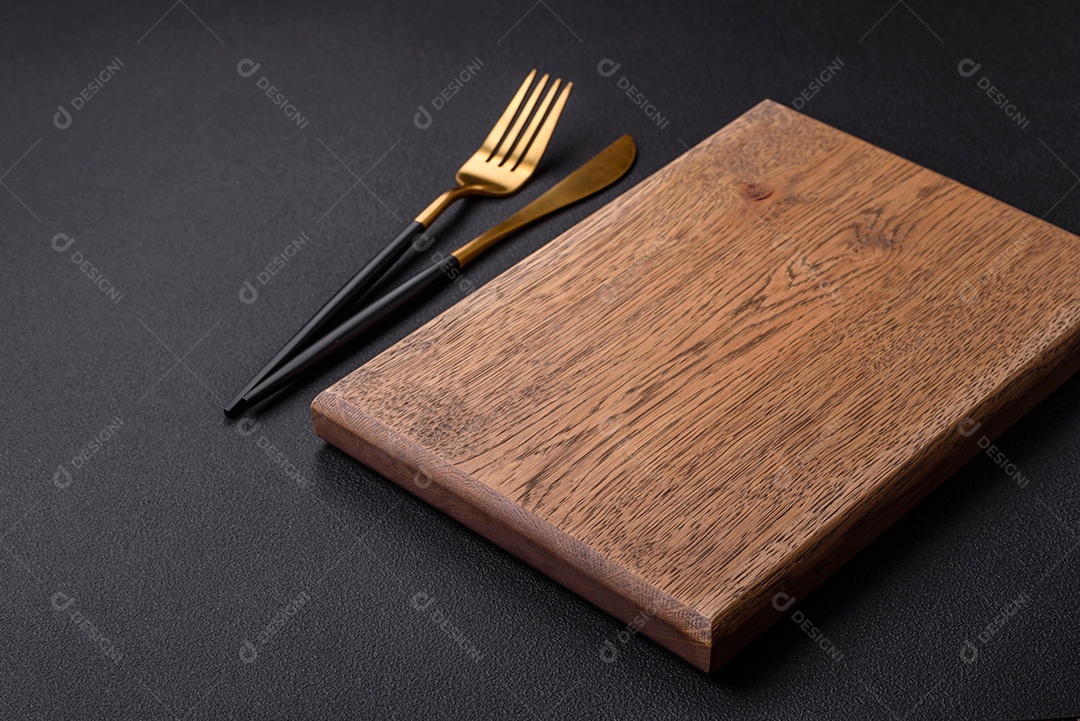 Tábua de corte de madeira vazia em fundo de concreto texturizado escuro. Talheres, preparação para o jantar