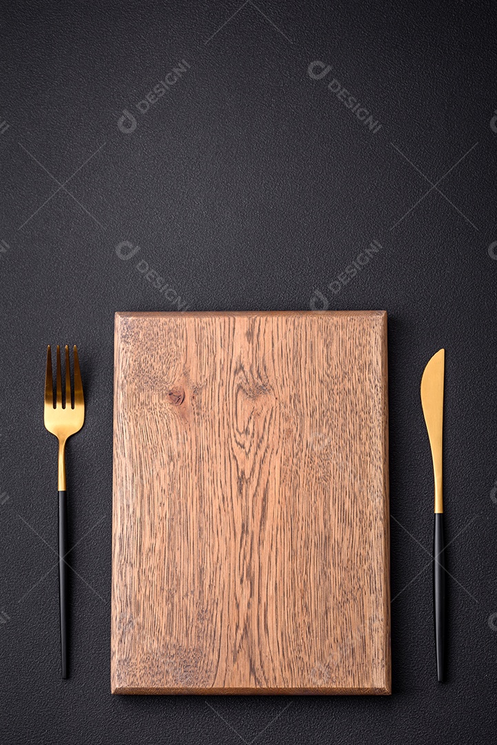 Tábua de corte de madeira vazia em fundo de concreto texturizado escuro. Talheres, preparação para o jantar