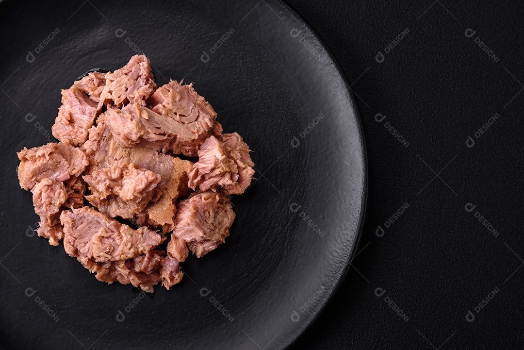 Deliciosa carne de atum enlatada em uma placa de cerâmica preta sobre um fundo escuro de concreto. Preparação de alimentos saudáveis