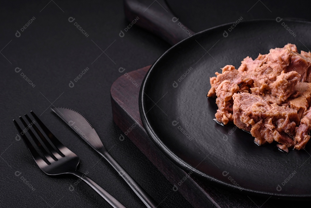 Deliciosa carne de atum enlatada em uma placa de cerâmica preta sobre um fundo escuro de concreto. Preparação de alimentos saudáveis