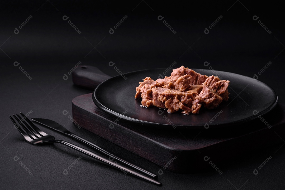 Deliciosa carne de atum enlatada em uma placa de cerâmica preta sobre um fundo escuro de concreto. Preparação de alimentos saudáveis