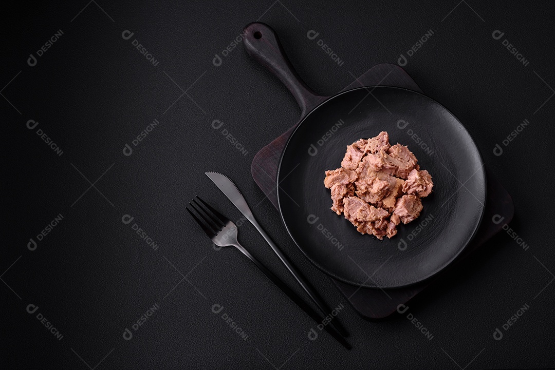 Deliciosa carne de atum enlatada em uma placa de cerâmica preta sobre um fundo escuro de concreto. Preparação de alimentos saudáveis