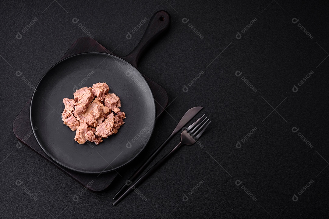 Deliciosa carne de atum enlatada em uma placa de cerâmica preta sobre um fundo escuro de concreto. Preparação de alimentos saudáveis